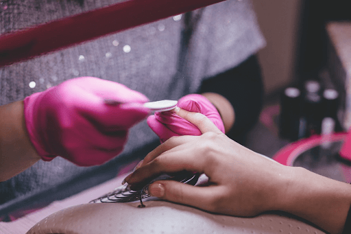 pink gloves giving a manicure to a lady’s hand