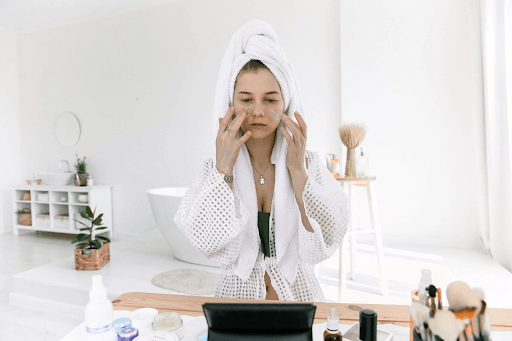 woman applying skincare with makeup and skincare products surrounding her
