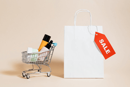 white paper bag with a red “SALE” tag, and a small pushcart with cosmetics in it