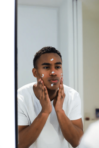 man in white shirt applying skincare products on his skin (men’s personal care image)