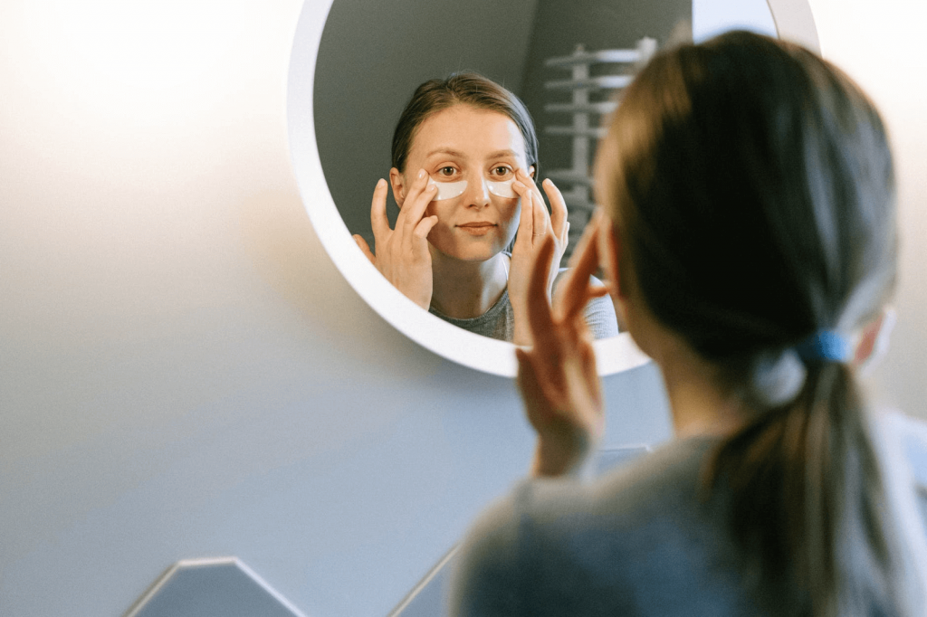 woman looking at herself in the mirror adding under eye patches