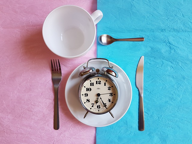  A silver alarm clock on a plate along with a teaspoon, fork, knife, and empty cup