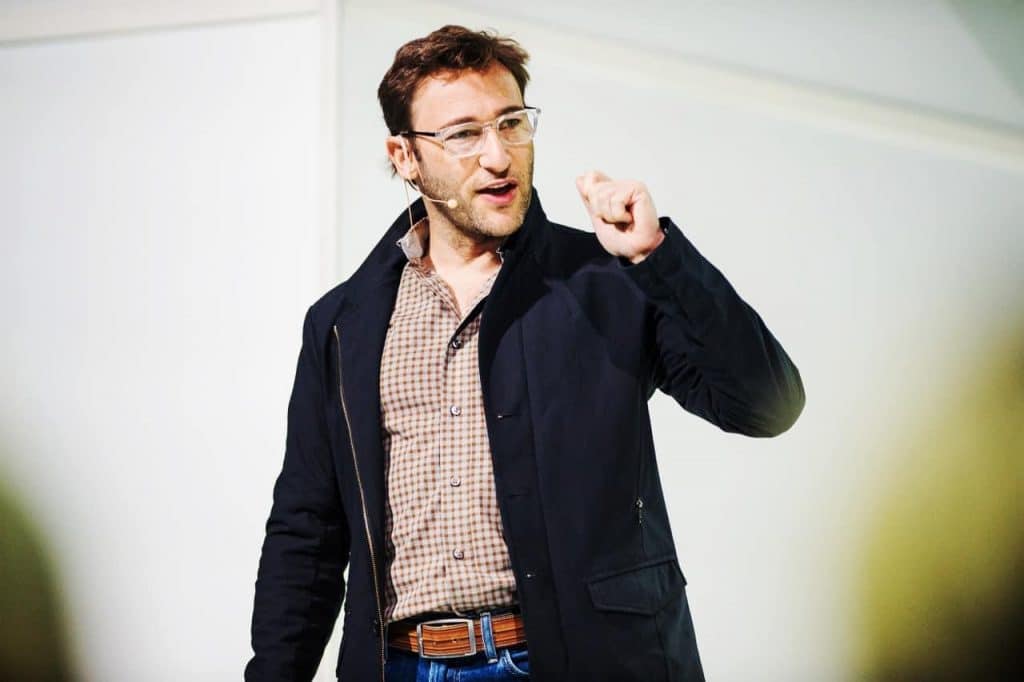 Simon Sinek in a black coat with a pleated top speaking for nbforum