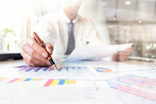 A businessman in a while polo holding a pen over a printed bar graph on the table