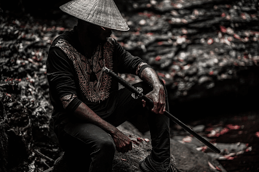 Man in black top and jeans and white sun hat holding a samurai sword