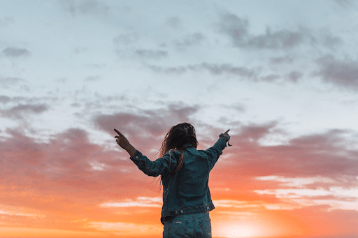 Faceless woman pointing with fingers at the bright sky in twilight