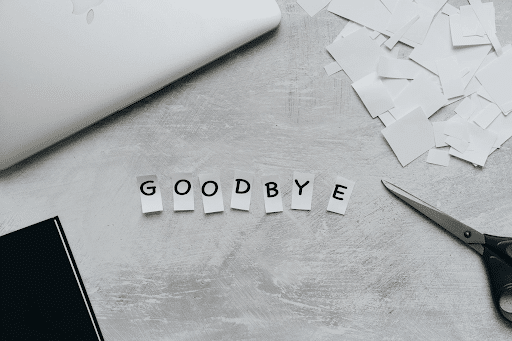 Cut GOODBYE letters, scissors, laptop, and pieces of paper on a grey table