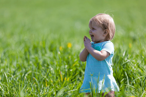 A baby girl wearing a green dress on a green grass field