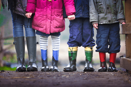 Lower bodies of four kids wearing muddy boots