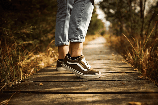 Feet of a person walking on a wooden path surrounded by grasses and trees
