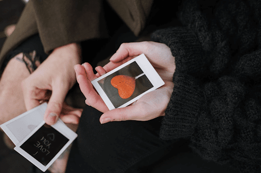 : Couple holding instant photos of a heart-shaped lollipop and “I LOVE YOU”