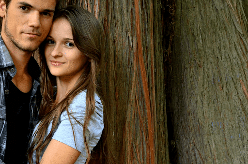 Young couple smiling while leaning on a tree
