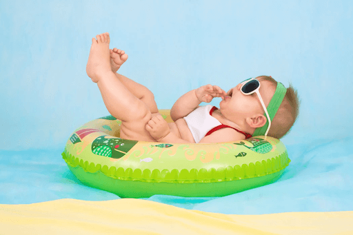 A baby wearing sunglasses lying on a green inflatable ring on a blue background