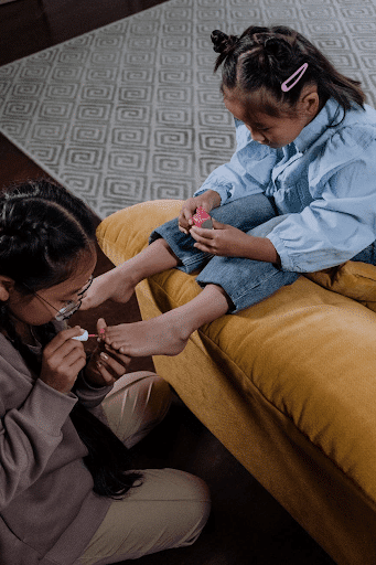 girl sitting on a brown sofa having her foot pedicured by her sister (crazy sister image)