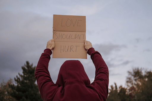 A man in a red hoodie holding a placard that says ‘love shouldn’t hurt’