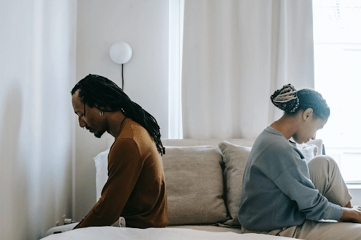 Black couple sitting opposite a bed with their backs on each other