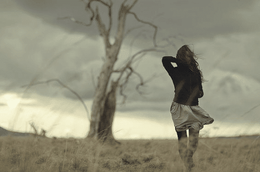 Woman walking towards a leafless tree on a barren land