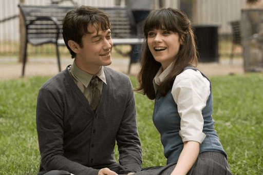 Tom and Summer sitting on a grassy ground with Tom looking at a laughing summer