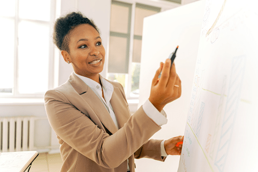 A businesswoman in a beige suit holding a highlighter in front of a whiteboard