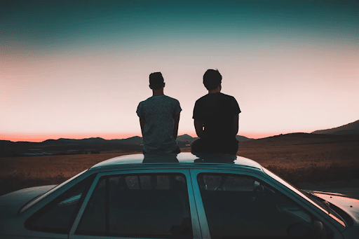 Two men seating on a vehicle parked on a road near a brown grass field