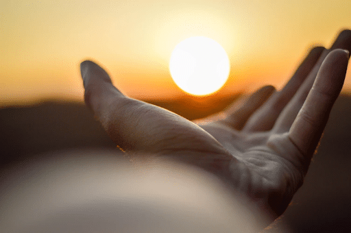 A man’s hand that seems to be holding the rising sun on his palms