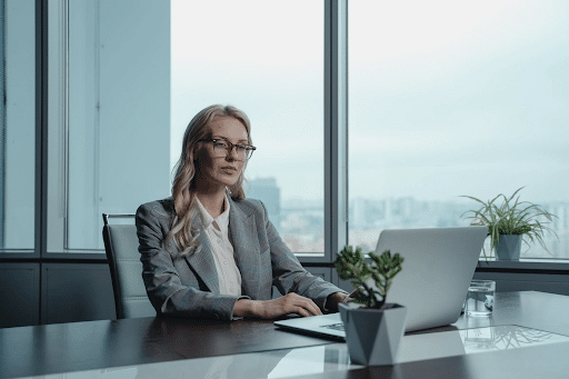 Blonde woman in a white shirt and gravy blazer sitting in front of a laptop