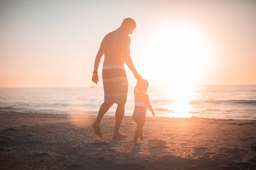  father and daughter holding hands and walking on the beach towards the sea