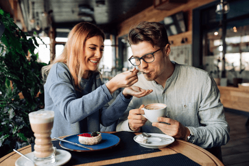 sweet picture of a woman feeding a man while the man holds a cup of coffee