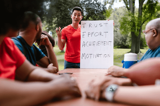 A man in a red shirt talking about Trust, Effort, Achievement, and Motivation (TEAM) in front of other people