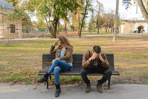 Woman and a man with hands on his head sitting on a brown wooden bench