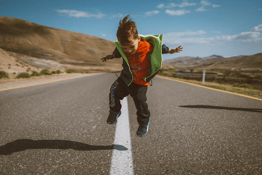 A little boy jumping on a concrete road in a barren place