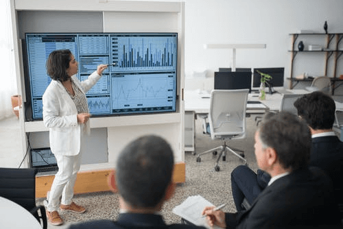  Woman in White Suit Discussing Stock Market Data to Her Colleague