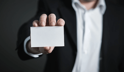 A man in a back suit holding a white business card