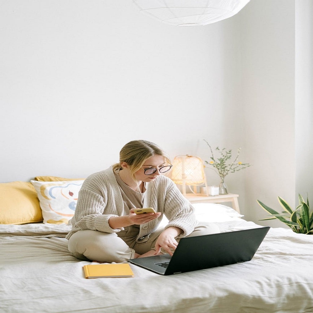 Woman Sitting on Bed While Using Black Laptop